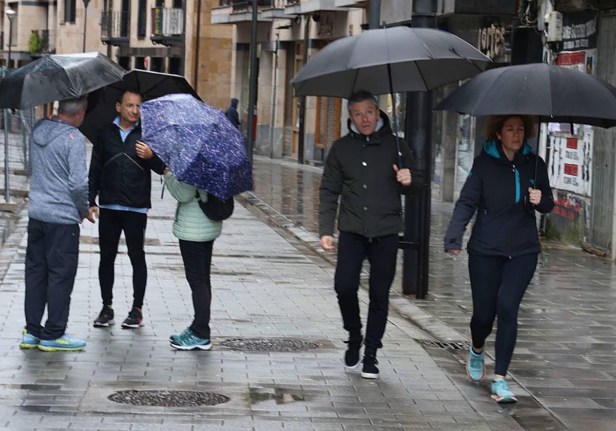 Dos personas pasean y tres conversan mientras llueve en Beasain.
