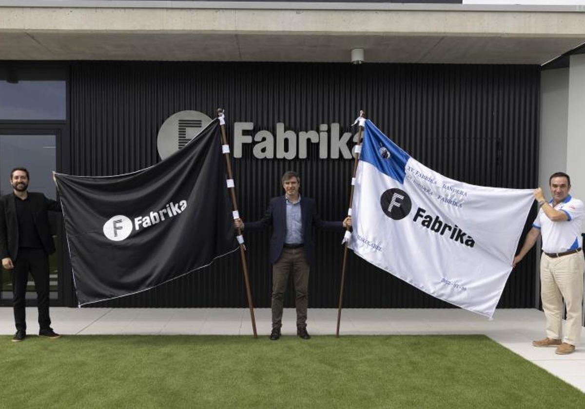 Iñaki Gabarain, nuevo concejal de Deportes del Ayuntamiento de San Sebastián, Juan Mancisidor, director de Fabrika y Alberto López, presidente de Kaiarriba-Donostiarra, posan con la Bandera Fabrika que se disputa este sábado.