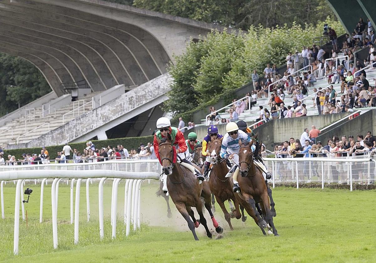 Los participantes en una carrera toman la curva frente a la tribuna del hipódromo.