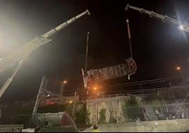 Uno de los vagones volcados en Pasaia es elevado por dos grandes grúas la madrugada de ayer.