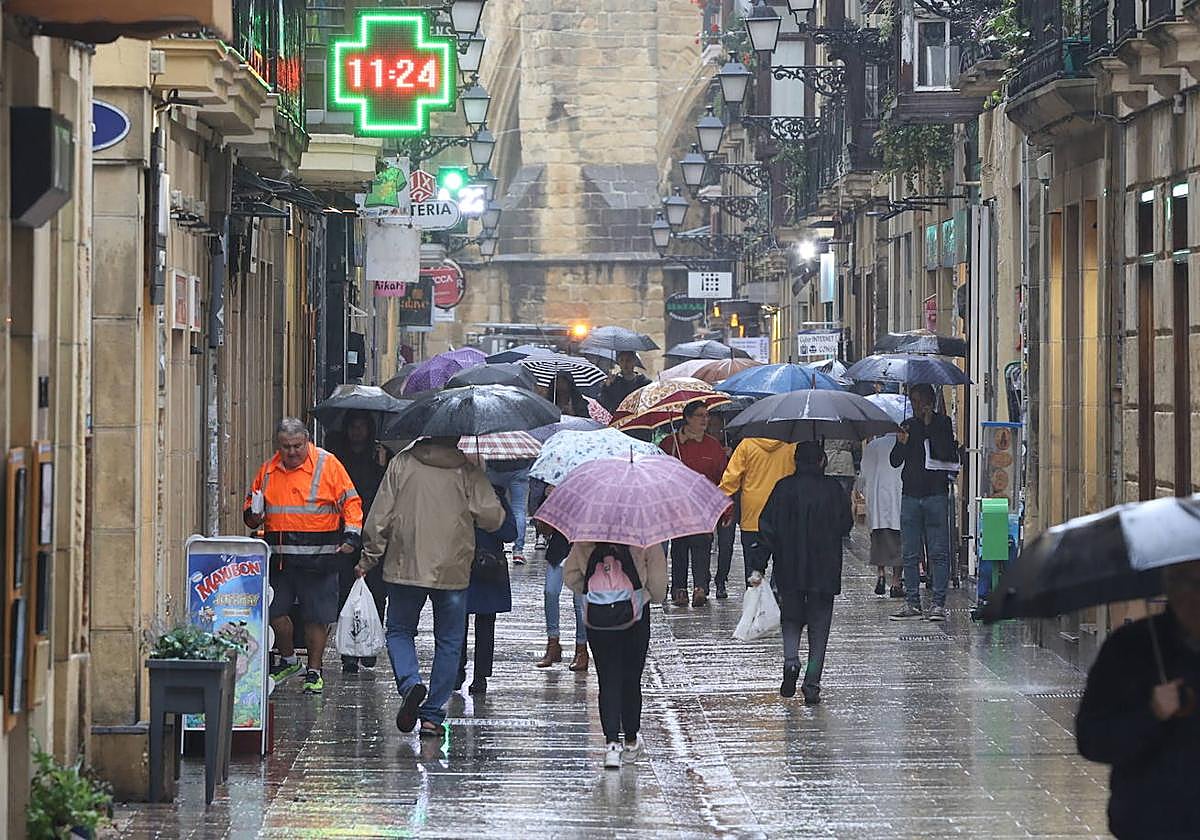 Varias personas pasean en la Parte Vieja de San Sebastián pertrechados contra lluvia.