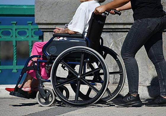 Un hombre lleva a una mujer dependiente en una silla de ruedas en Donostia.