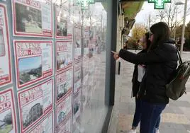 Dos jóvenes inspeccionan los anuncios de una inmobiliaria de Irun.