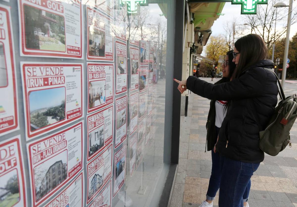 Dos jóvenes inspeccionan los anuncios de una inmobiliaria de Irun.