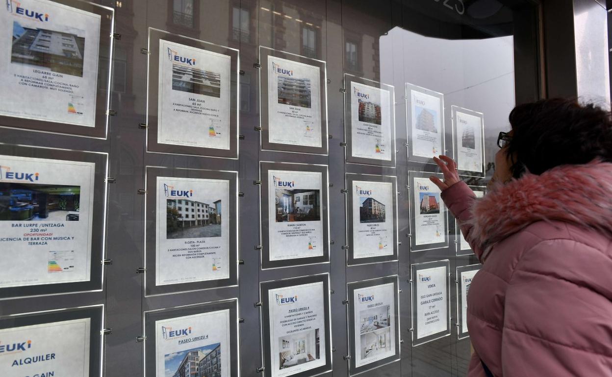 Una mujer observa varios anuncios de viviendas en venta y alquiler en una inmobiliaria. 