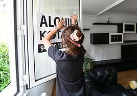 Una agente inmobiliaria coloca un cartel en una ventana para poner una vivienda en alquiler en Eibar.