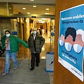 Dos pacientes abandonan el área de consultas externas del Hospital Donostia frente a un cartel que avisa de la obligatoriedad de portar la mascarilla.