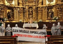 Una pancarta frente al altar donde se puede leer 'Iglesia avariciosa, especuladora!'.