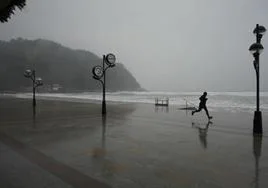 Un hombre corre en Zarautz bajo la lluvia.