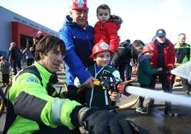 Un niño sujeta una manguera con la ayuda de un bombero.