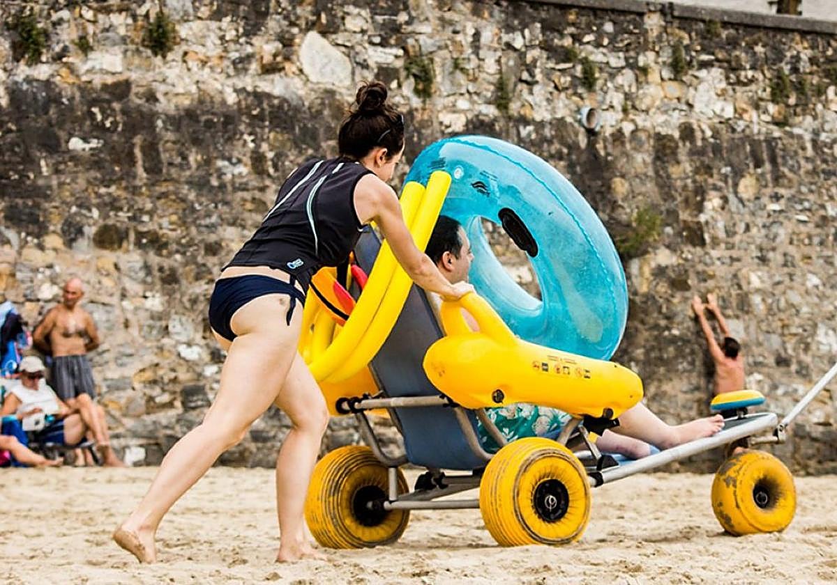 Un hombre con necesidades de baño adaptado es conducido a la orilla en la playa de Malkorbe en Getaria.