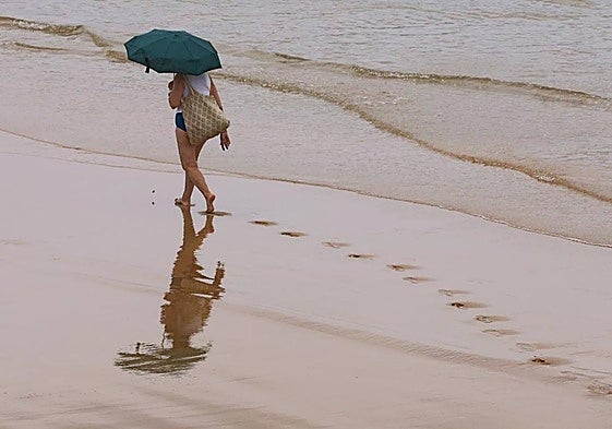 Una persona pasea por la orilla en un día lluvioso.