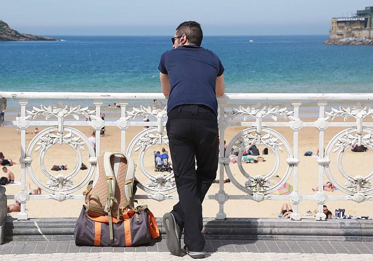 Un turista contempla la bahía donostiarra apoyado en la barandilla de La Concha.