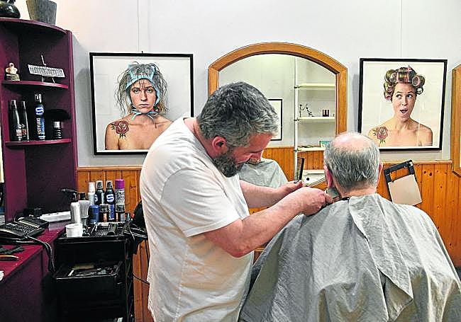 Peluquería Juan Cruz. El peluquero atiende a un cliente con las obras de arte como testigo.