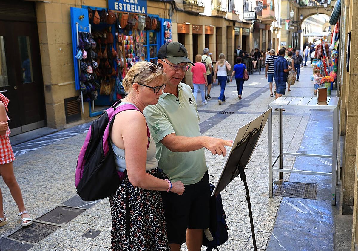 Dos turistas leen la carta de un restaurante en la Parte Vieja donostiarra.