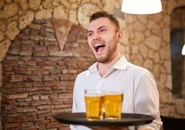 Un camarero sirviendo un par de vasos de cerveza.