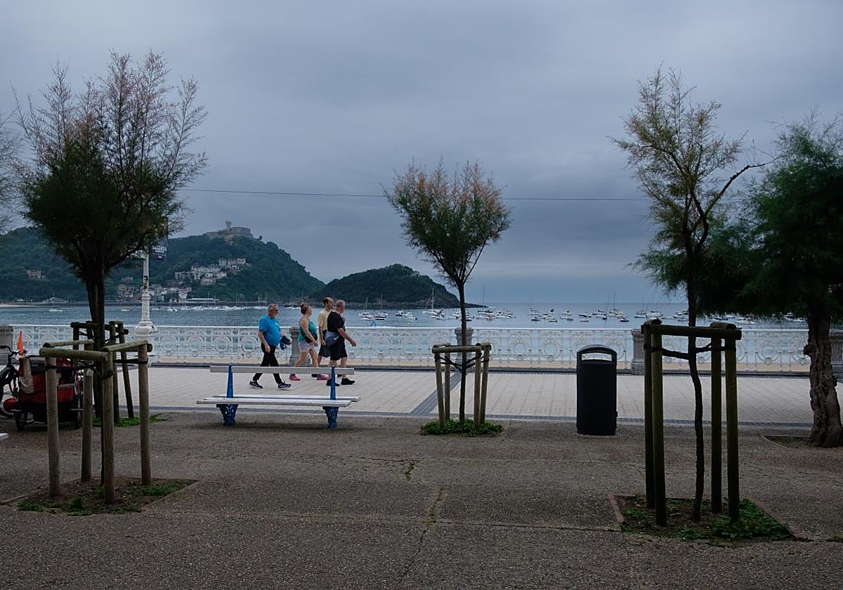 Tres hombres y una mujer caminan por el paseo de La Concha con el cielo nublado.