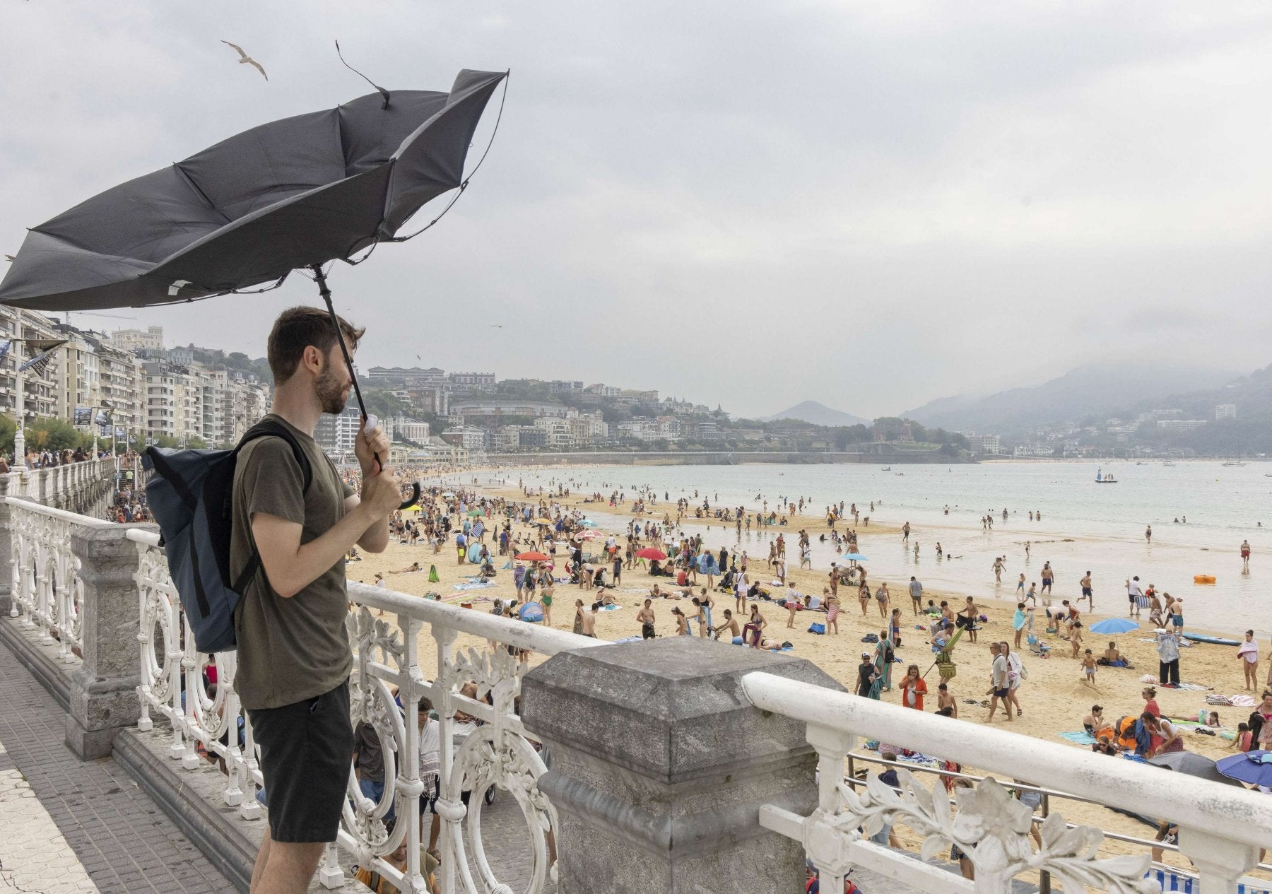 Un paseante con paraguas un día de verano en La Concha.