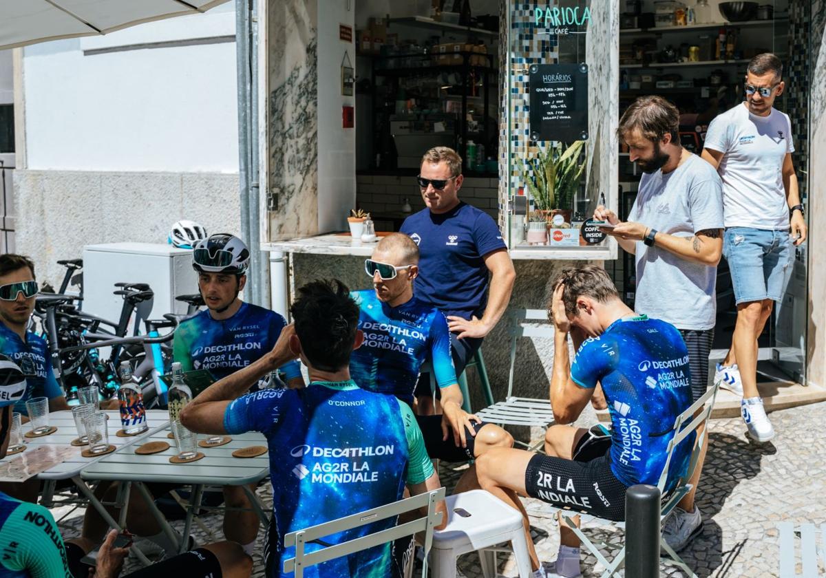 Los ciclistas del Decathlon, relajados tomando algo en una terraza con Ben O'Connor en primer plano, de espaldas.