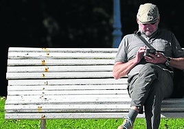 Un hombre consulta su teléfono móvil sentado en un banco de la ciudad.