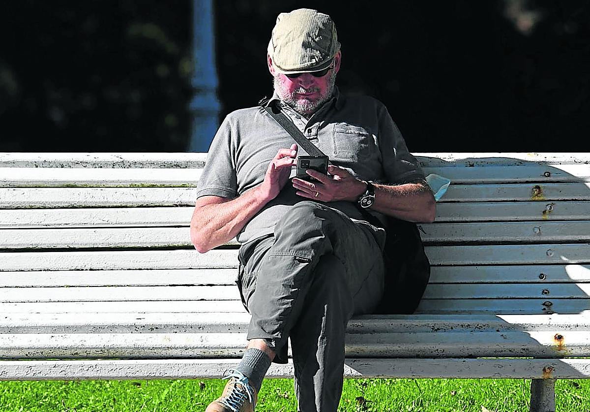 Un hombre consulta su teléfono móvil sentado en un banco de la ciudad.