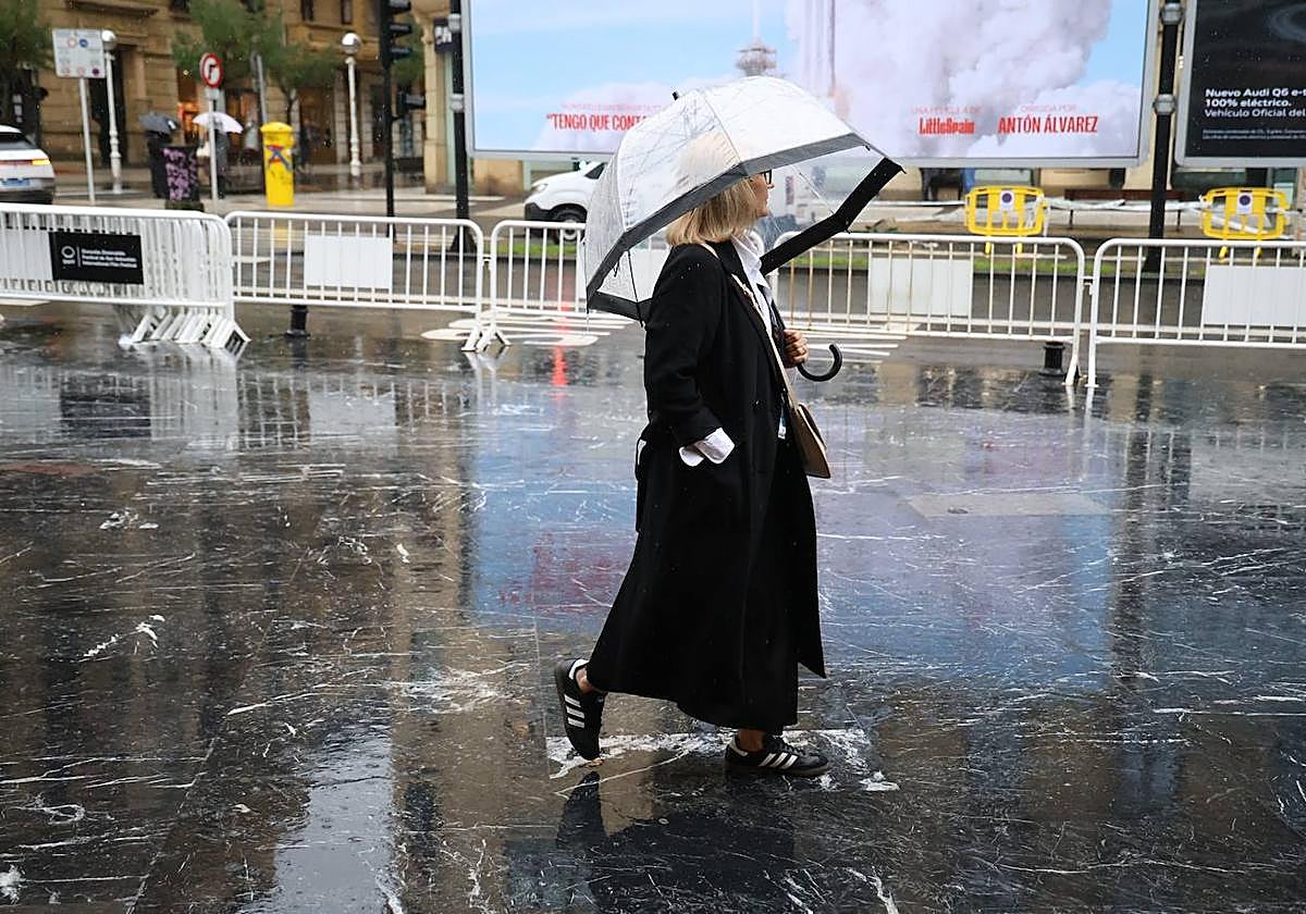 Una mujer pasea con paraguas por una calle de San Sebastián.