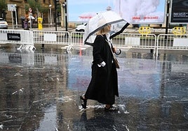 Una mujer pasea con paraguas por una calle de San Sebastián.