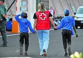 Una voluntaria de la Cruz Roja acompaña a dos menores extranjeros recién llegados a la isla de El Hierro, en Canarias.