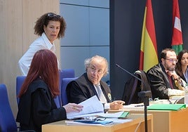 La abogada de la acusada pasa por detrás de la abogada del acusado, sentada y de espaldas, con el Fiscal al fondo.