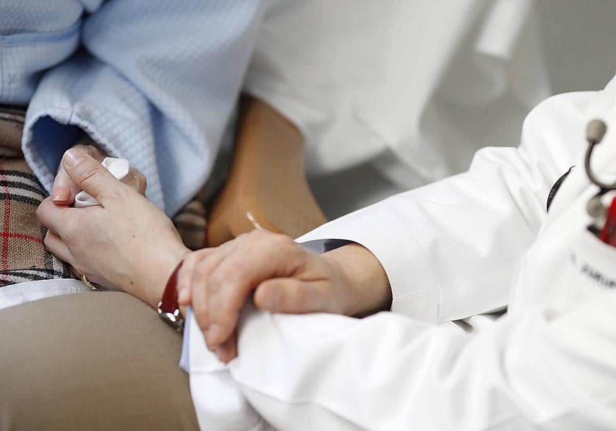 Una médico sostiene la mano de un paciente paliativo.