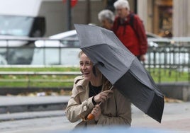 Una joven camina protegiéndose del viento y de la lluvia en San Sebastián