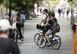 Varios jóvenes circulan en bicicleta por una acera del centro de San Sebastián.