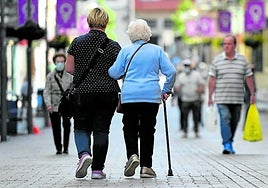 Una mujer mayor camina por la calle con una cuidadora.