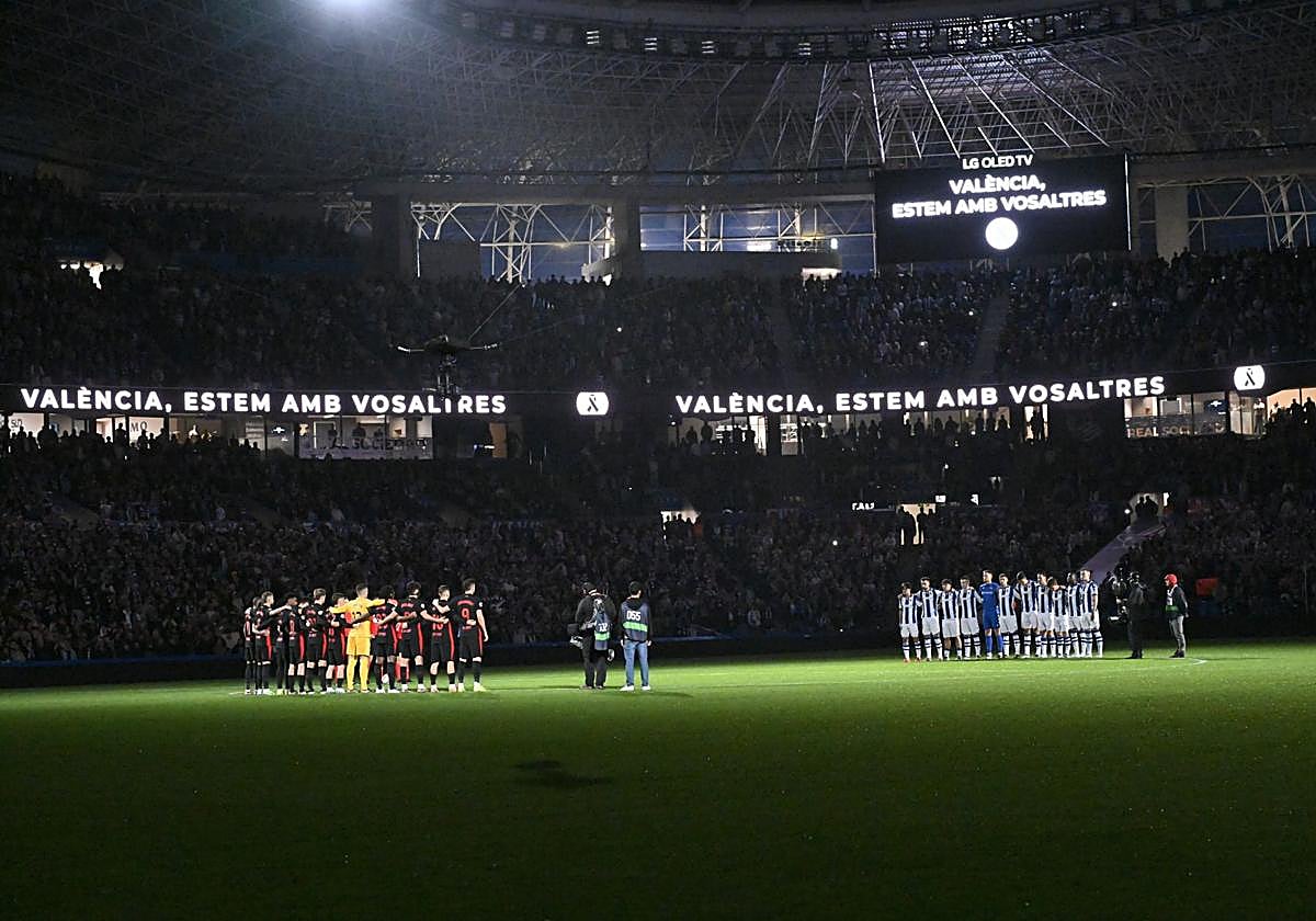 Los dos equipos abrazados en torno al círculo central durante el minuto de silencio con el Reale Arena a oscuras y el mensaje hacia los afectados por la DANA en el marcador.