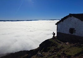 Un montañero fotografía junto a la ermita de Mendaur el denso manto de nubes que cubre el valle.