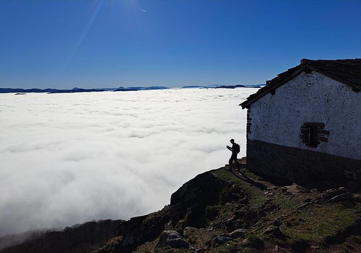 Un montañero fotografía junto a la ermita de Mendaur el denso manto de nubes que cubre el valle.