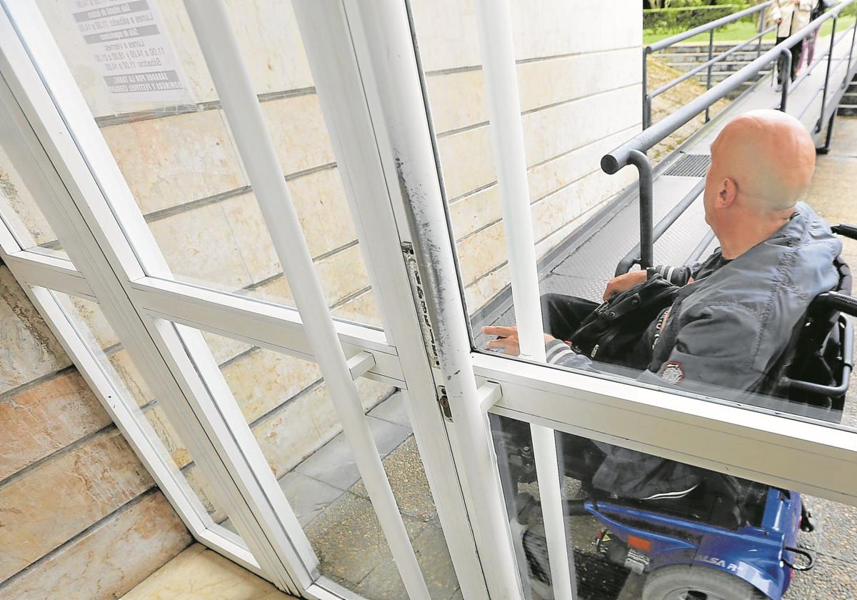 Un hombre en silla de ruedas ante la puerta de un edificio con rampa de acceso para personas con dificultades de movilidad.