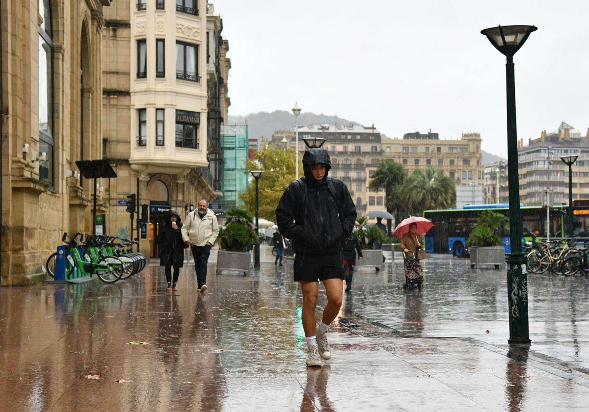 Un joven camina bajo la lluvia sin paraguas.