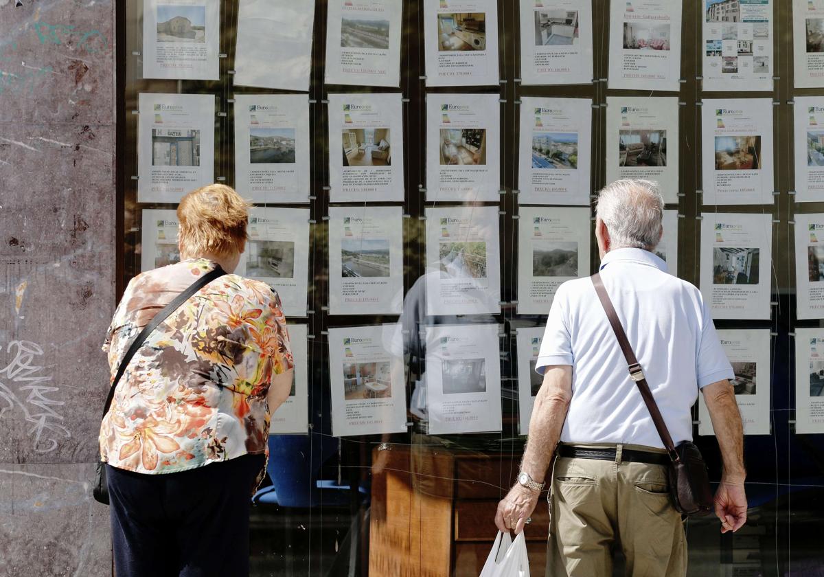 Dos personas miran anuncios de pisos en una inmobiliaria de Errenteria.