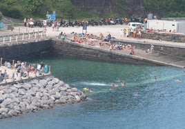 Numerosas personas disfrutan en torno a la vieja piscina de agua marina del puerto de Mutriku durante una jornada estival.