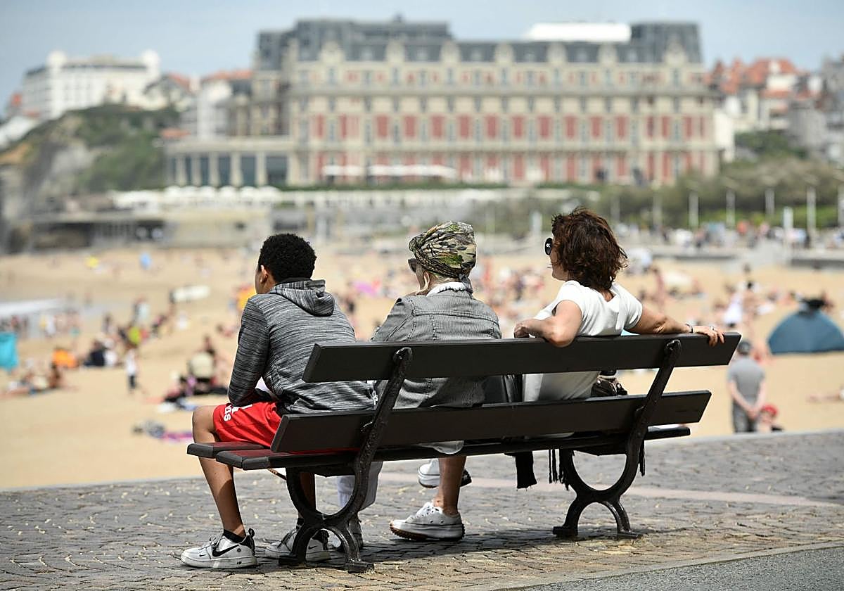Tres personas en un banco y el Hôtel du Palais de fondo en Biarritz.