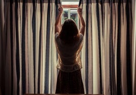 Una mujer cierra las cortinas de su casa.
