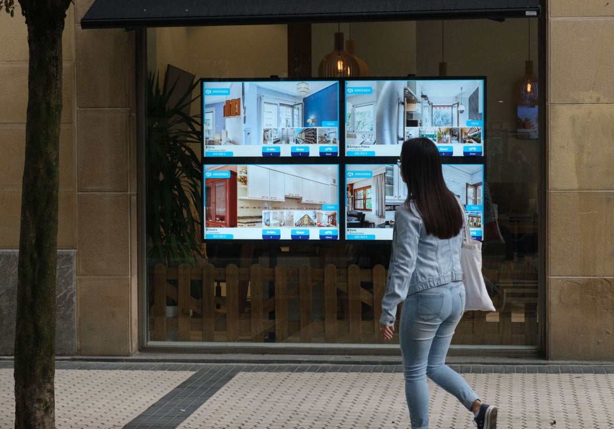 Una mujer joven pasa por delante de una inmobiliaria en Donostia.