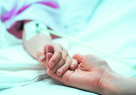 Un familiar sostiene la mano de un paciente paliativo en un hospital.