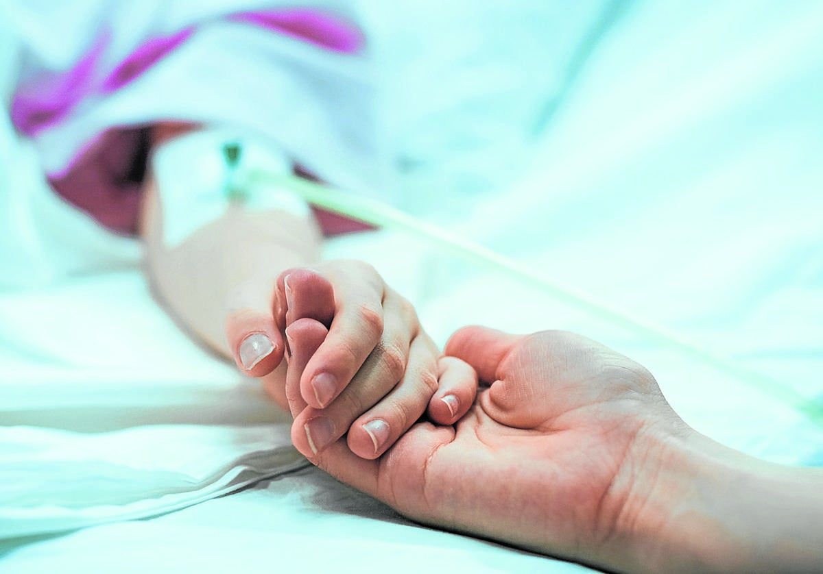 Un familiar sostiene la mano de un paciente paliativo en un hospital.
