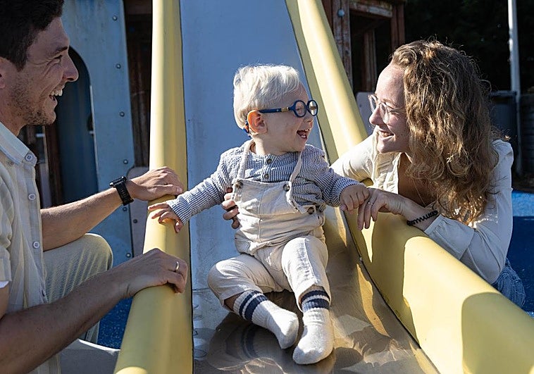 Álex y Janita juegan con Marco, sonriente mientras se tira con la ayuda de sus padres por un tobogán.