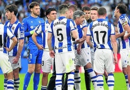 Imanol charla con Mikel Oyarzabal ante la mirada atenta del resto de la plantilla en un partido en Anoeta.