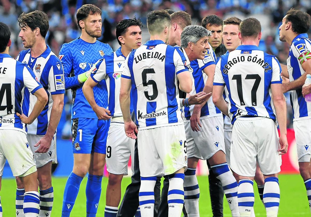 Imanol charla con Mikel Oyarzabal ante la mirada atenta del resto de la plantilla en un partido en Anoeta.