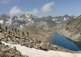 Los montañeros avanzan entre neveros y rocas rumbo al Pico Serrato, con el Ibón de Bachimaña y las cumbres del macizo de los Infiernos al fondo.