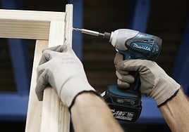 Un hombre utiliza un taladro atornillador para montar un mueble de madera.